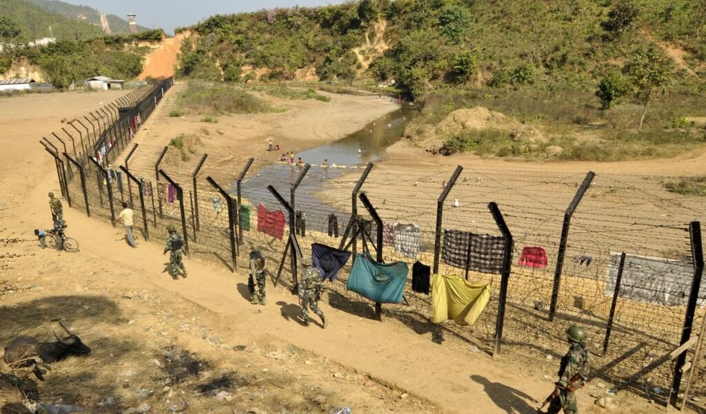 Security personnel and engineers overseeing fencing construction along the Indo-Myanmar border in a hilly forested region.