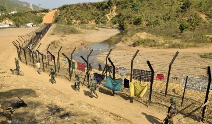 Security personnel and engineers overseeing fencing construction along the Indo-Myanmar border in a hilly forested region.