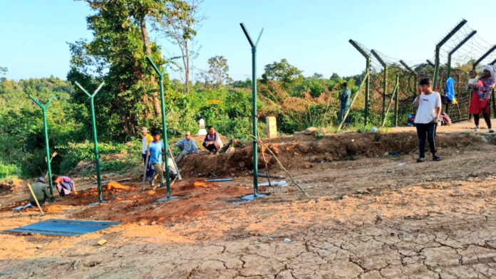 Security personnel and engineers supervising border fencing construction along the Indo-Myanmar frontier in a hilly terrain area.
