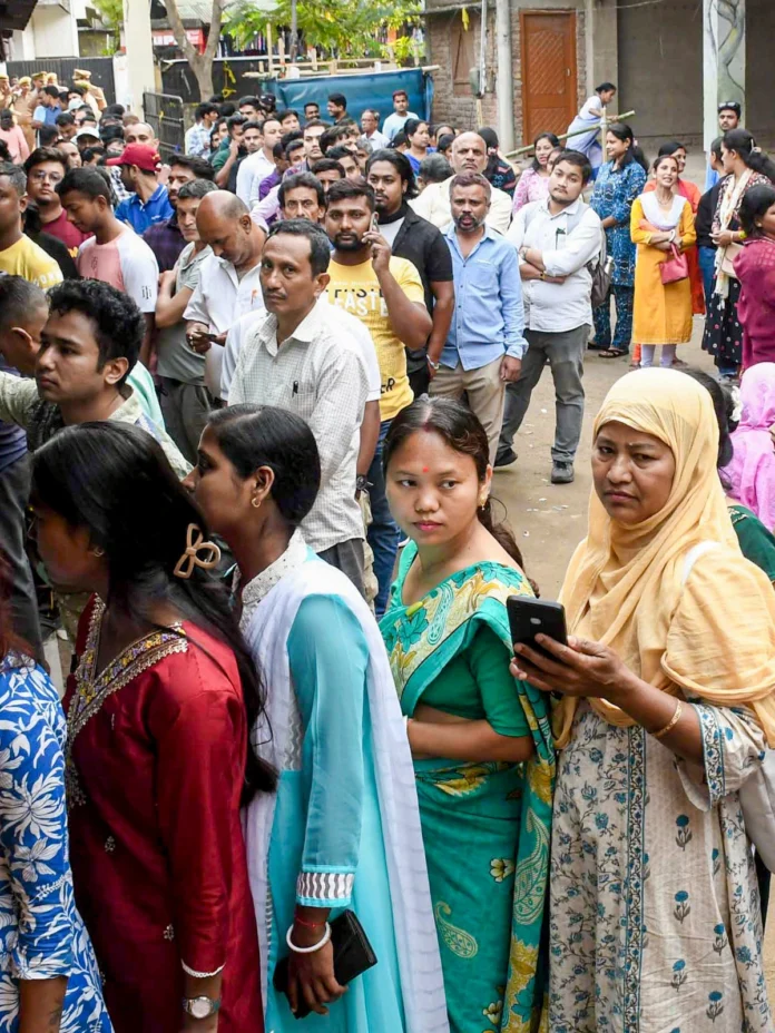 Voters queue outside a polling station in Assam during the Assembly elections, reflecting high electoral participation across the state.
