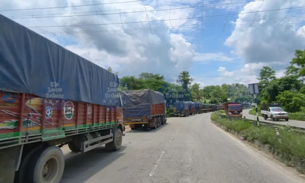 Commercial trucks queue along a landslide-affected stretch of NH-37 as transport unions raise concerns over alleged unauthorized toll collection and traffic delays.